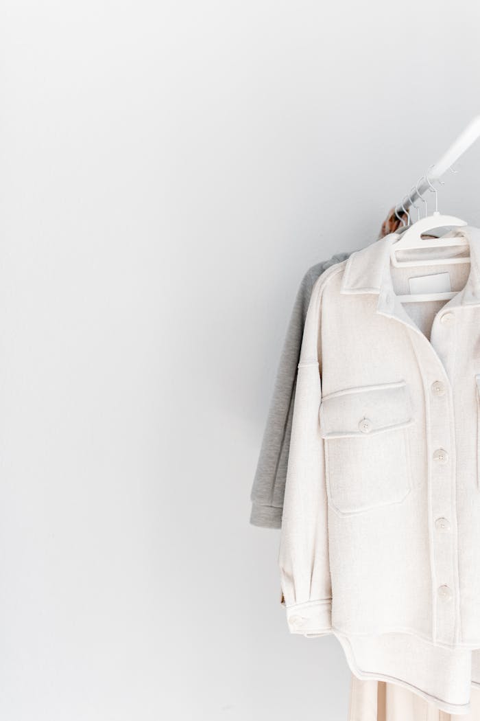 service-01 A minimalist wardrobe featuring neutral-tone clothes on hangers against a white background.