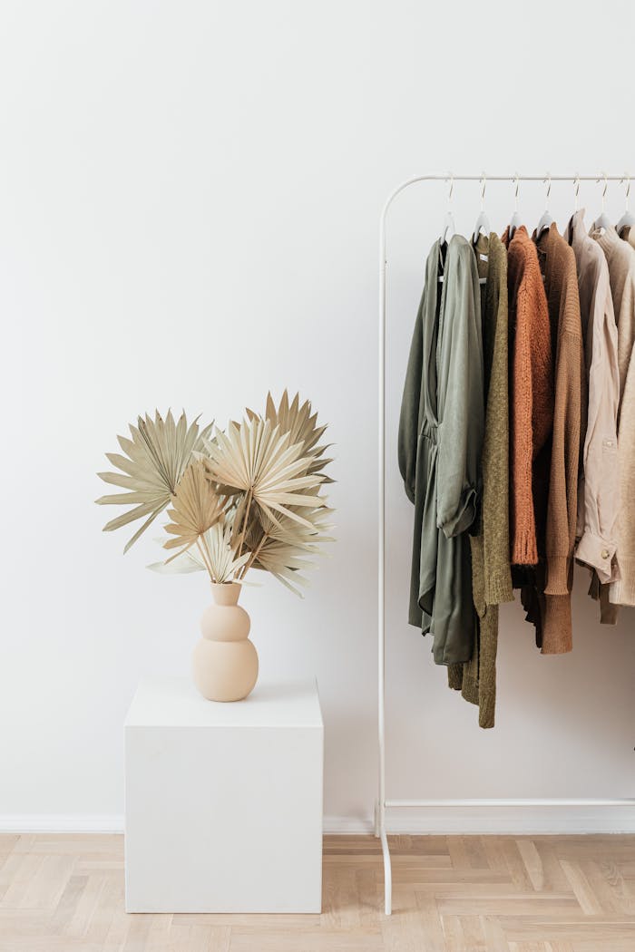 about-me-img A stylish minimalist clothing display on a rack with dried palm leaves in a vase.
