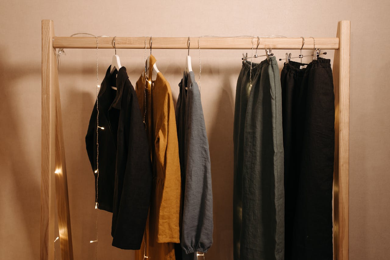 Natural fabric clothes hanging on a wooden rack in a minimalist style, enhanced with fairy lights for warmth.
