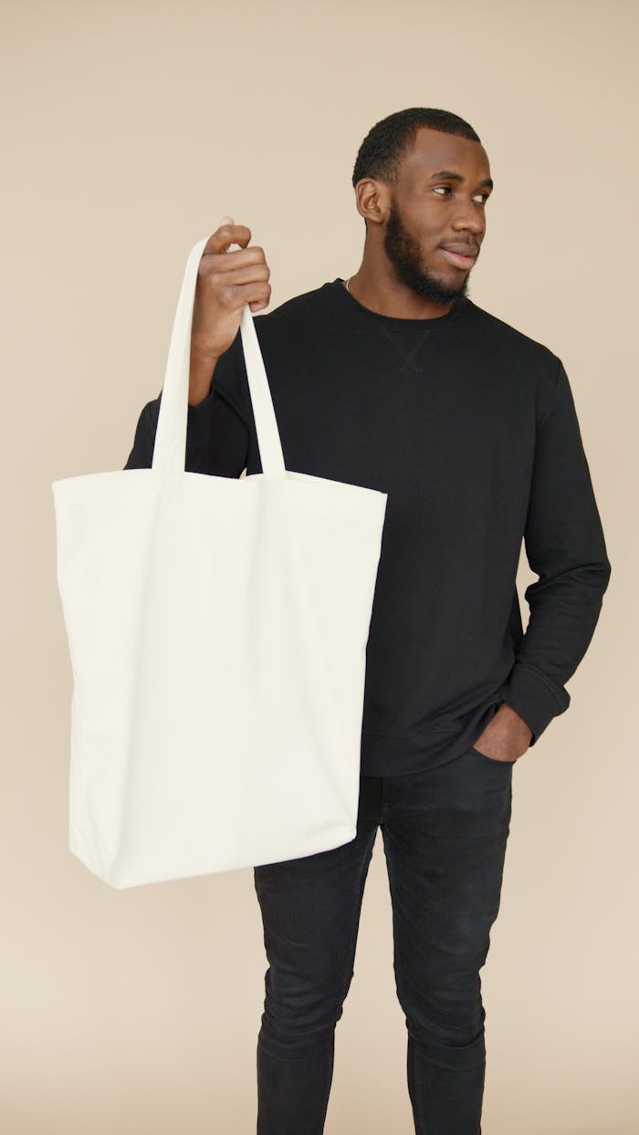 service-03 Fashionable man holding a minimalist white tote bag against a neutral background.